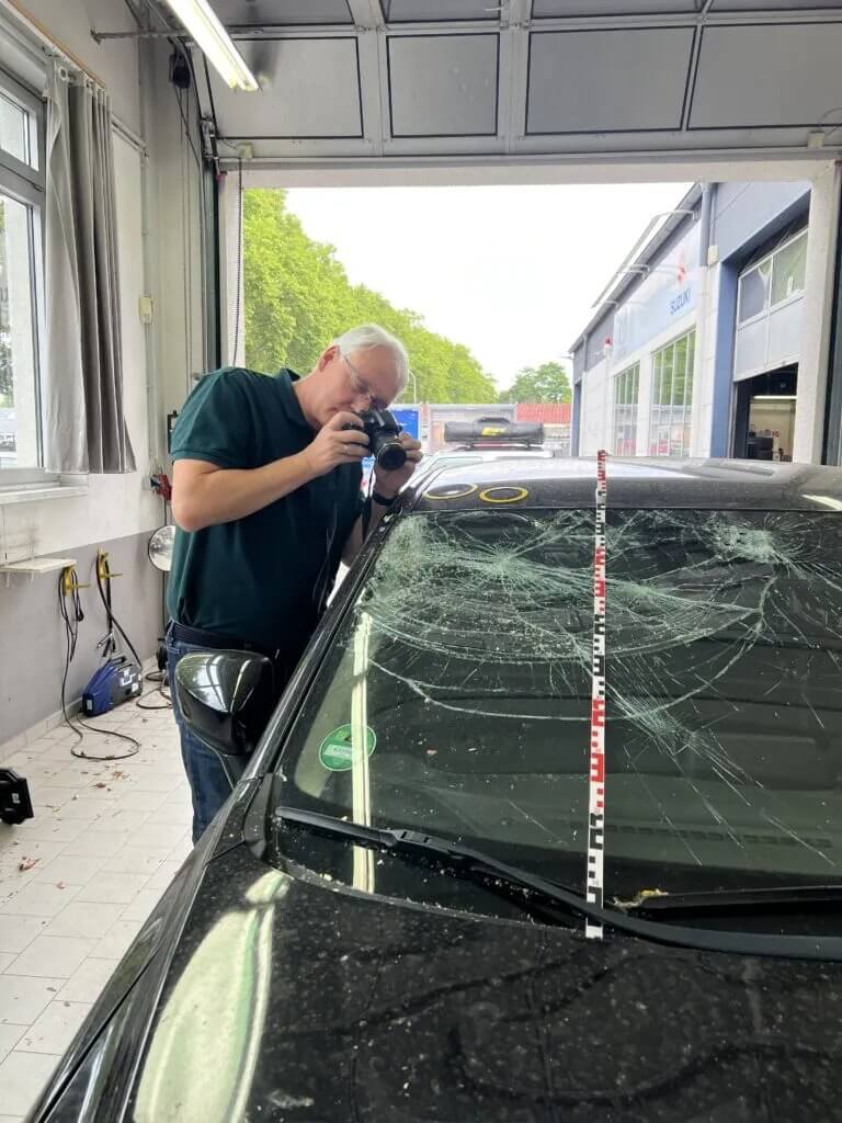 Ein Mann fotografiert eine stark zerklüftete Autoscheibe in einer Autowerkstatt