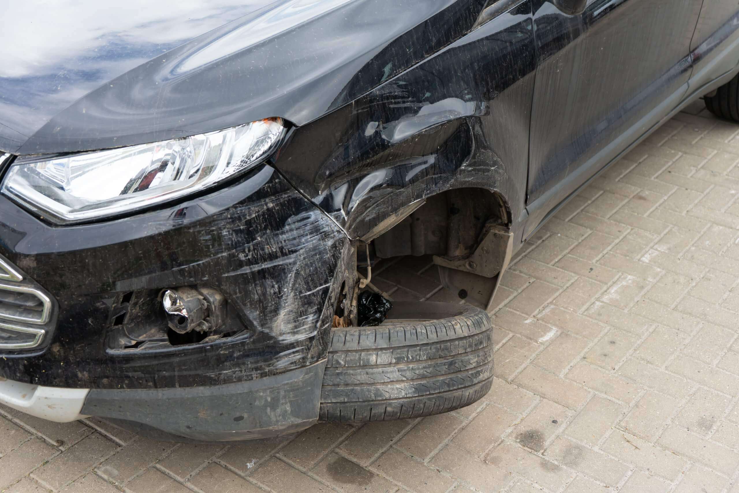 Schwarzes Auto mit starkem Frontschaden und abmontiertem Rad auf Ziegelsteinen, geeignet für ein Schadengutachten