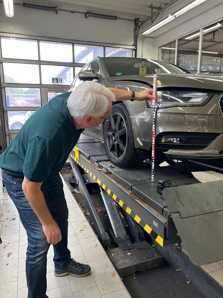 Ein Mann misst mit einem Messstab die Höhe der vorderen Stoßstange eines Autos in einer Autowerkstatt