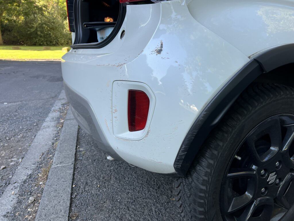 Ein weißer SUV mit Kratzern und Schmutz am hinteren Stoßfänger steht am Bordstein, der Kofferraum ist offen